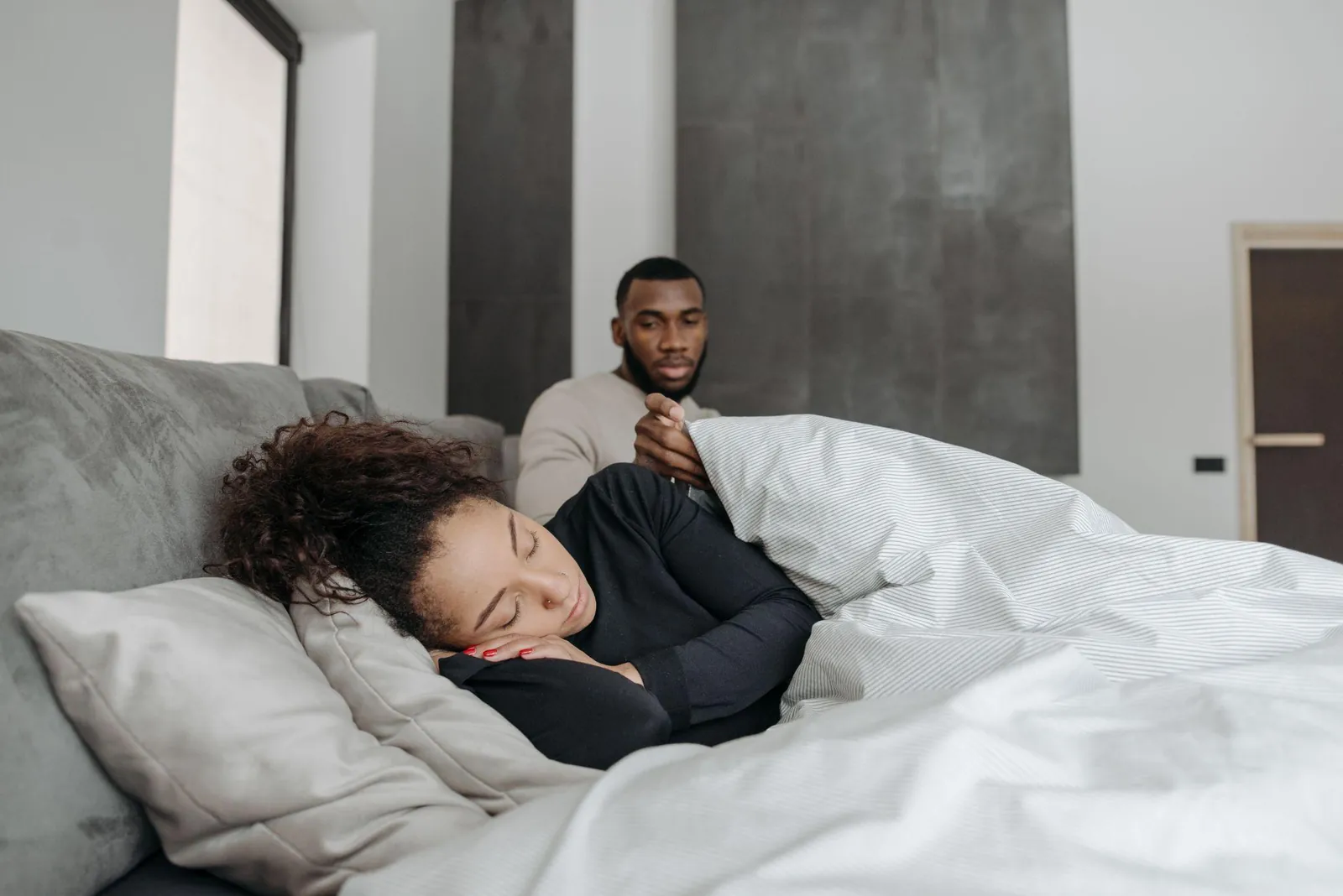 Una persona duerme plácidamente mientras su pareja la mira con preocupación desde el otro lado de la cama.